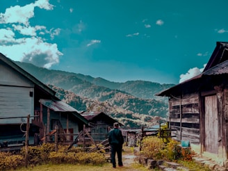 man in black jacket standing near brown wooden house during daytime