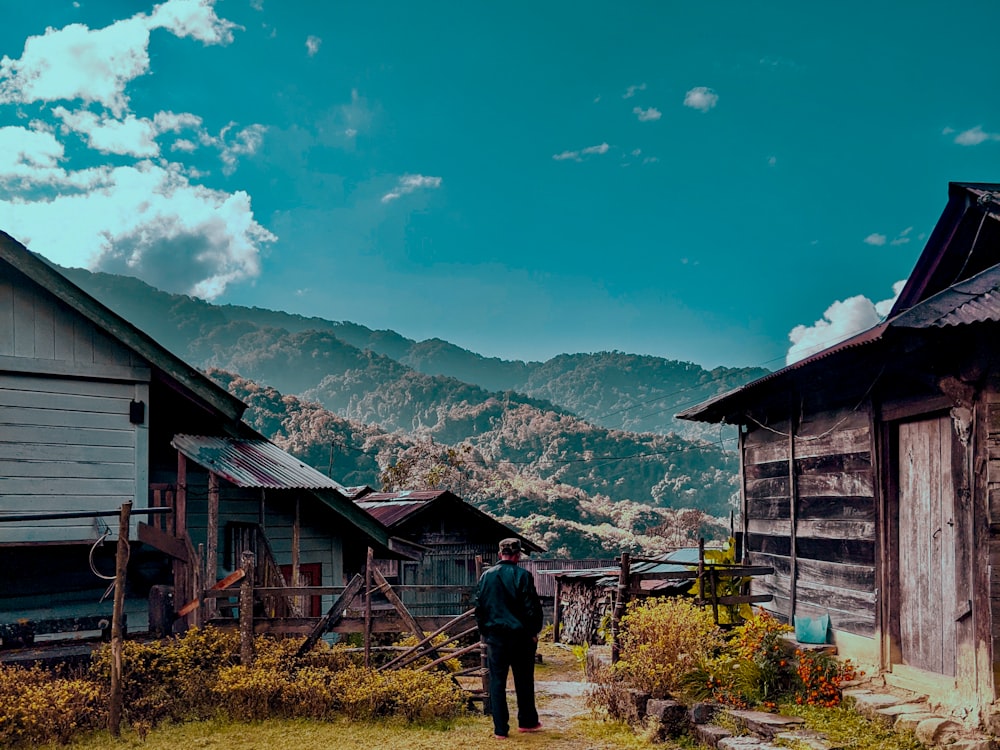 man in black jacket standing near brown wooden house during daytime