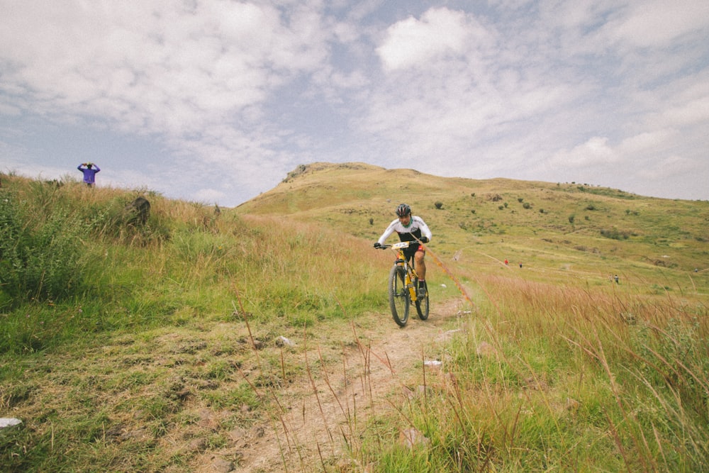 man in white shirt riding bicycle on green grass field during daytime