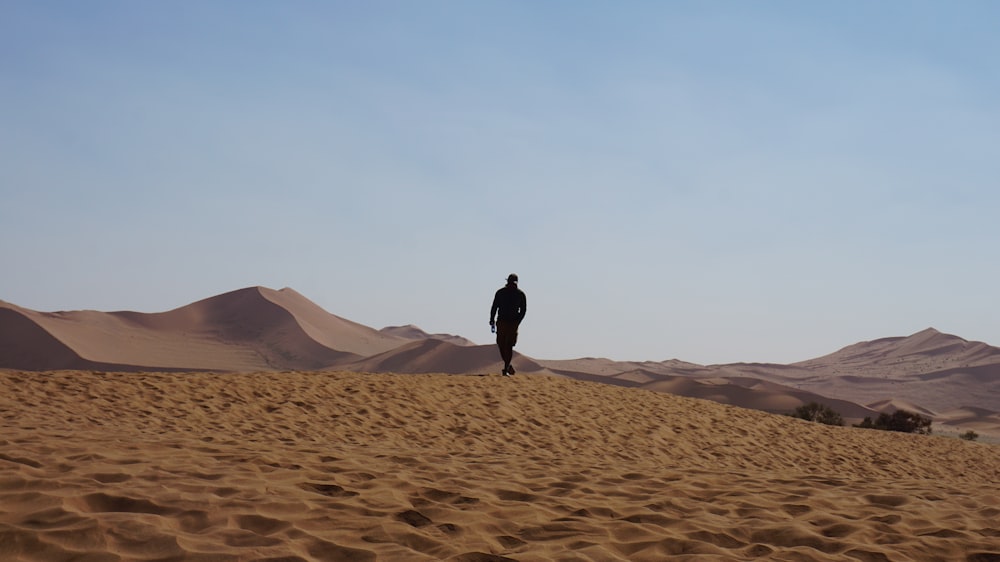 Uomo in giacca nera che cammina sulla sabbia marrone durante il giorno