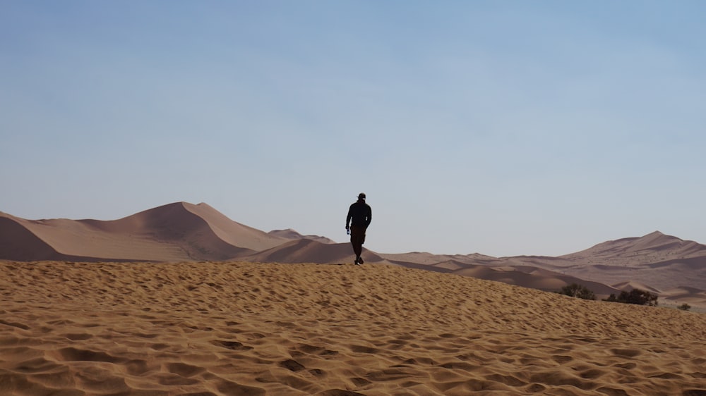 Hombre con chaqueta negra caminando sobre arena marrón durante el día