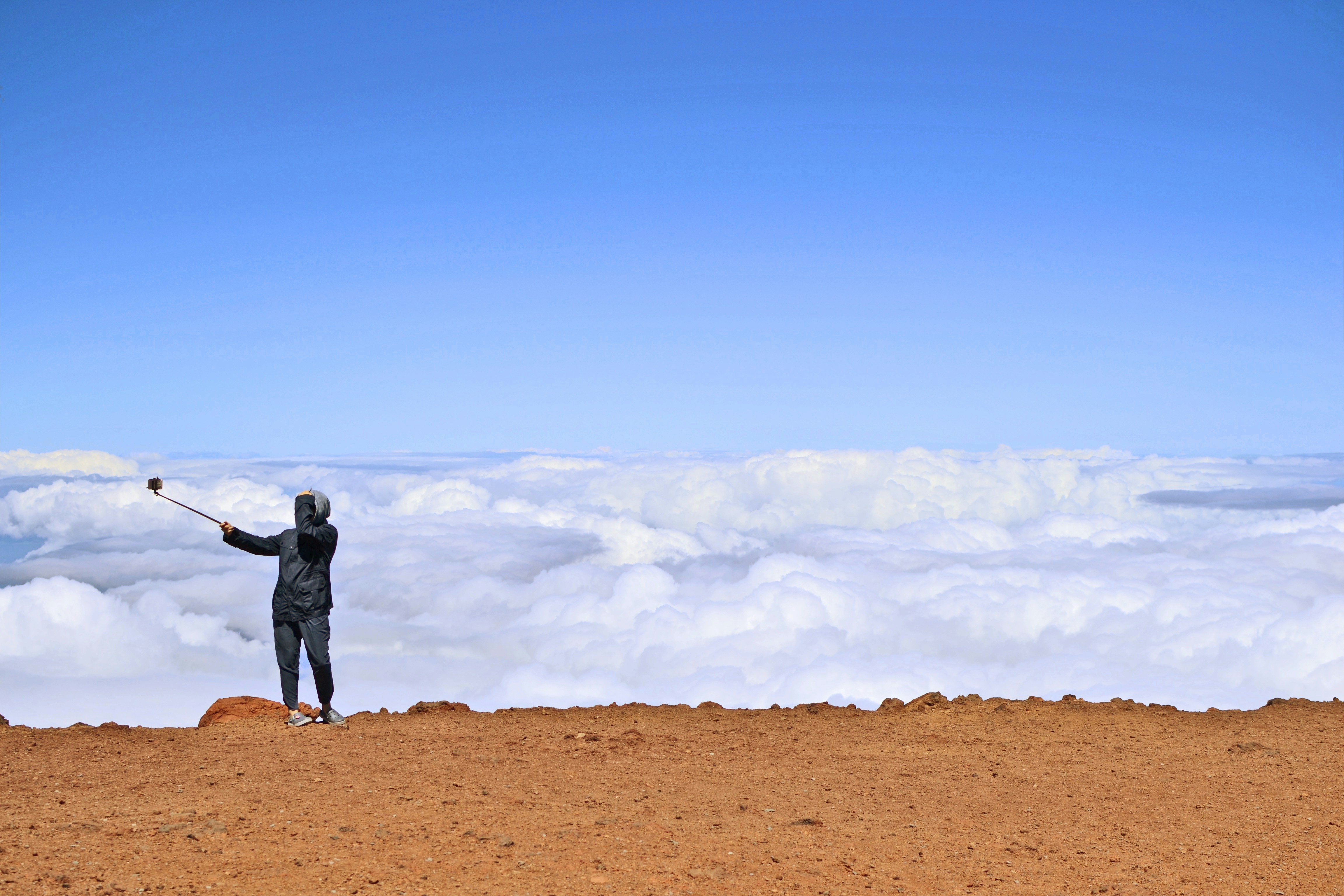 man in black jacket and pants standing on brown field under white clouds and blue sky