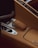 A close-up of a car's interior highlighting the gear selector encased in tan leather with distinctive stitching. The surrounding console is also covered with the same tan leather. A metallic knob and several buttons are visible, contributing to a luxurious automotive design.