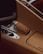 A close-up of a car's interior highlighting the gear selector encased in tan leather with distinctive stitching. The surrounding console is also covered with the same tan leather. A metallic knob and several buttons are visible, contributing to a luxurious automotive design.
