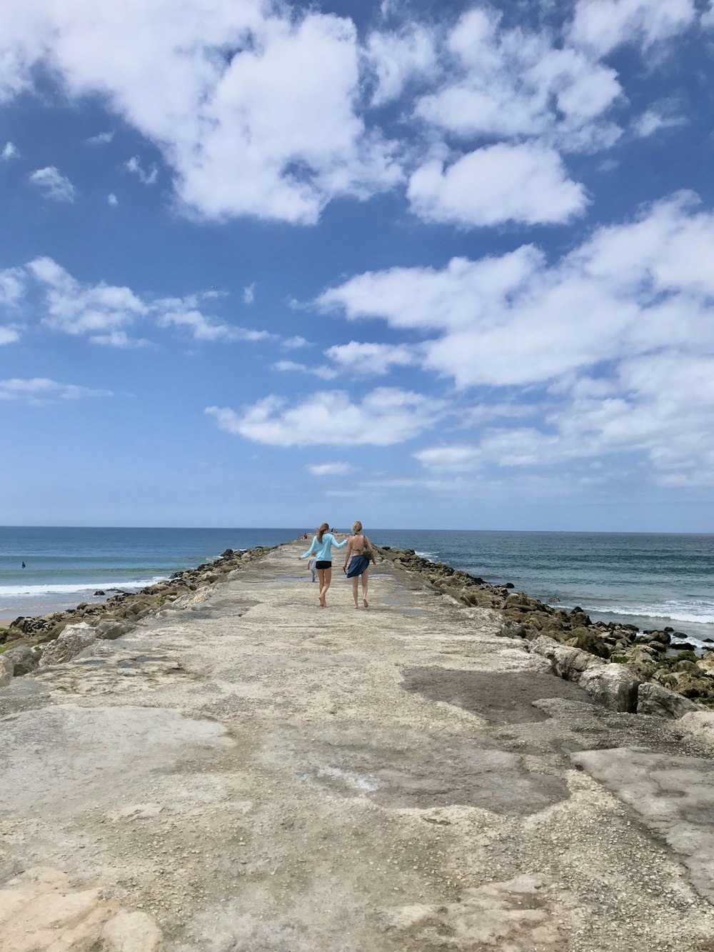 2 person walking on gray concrete pathway near body of water during daytime