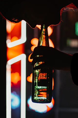 Close-up of a hand holding a chilled bottle with red neon reflections.