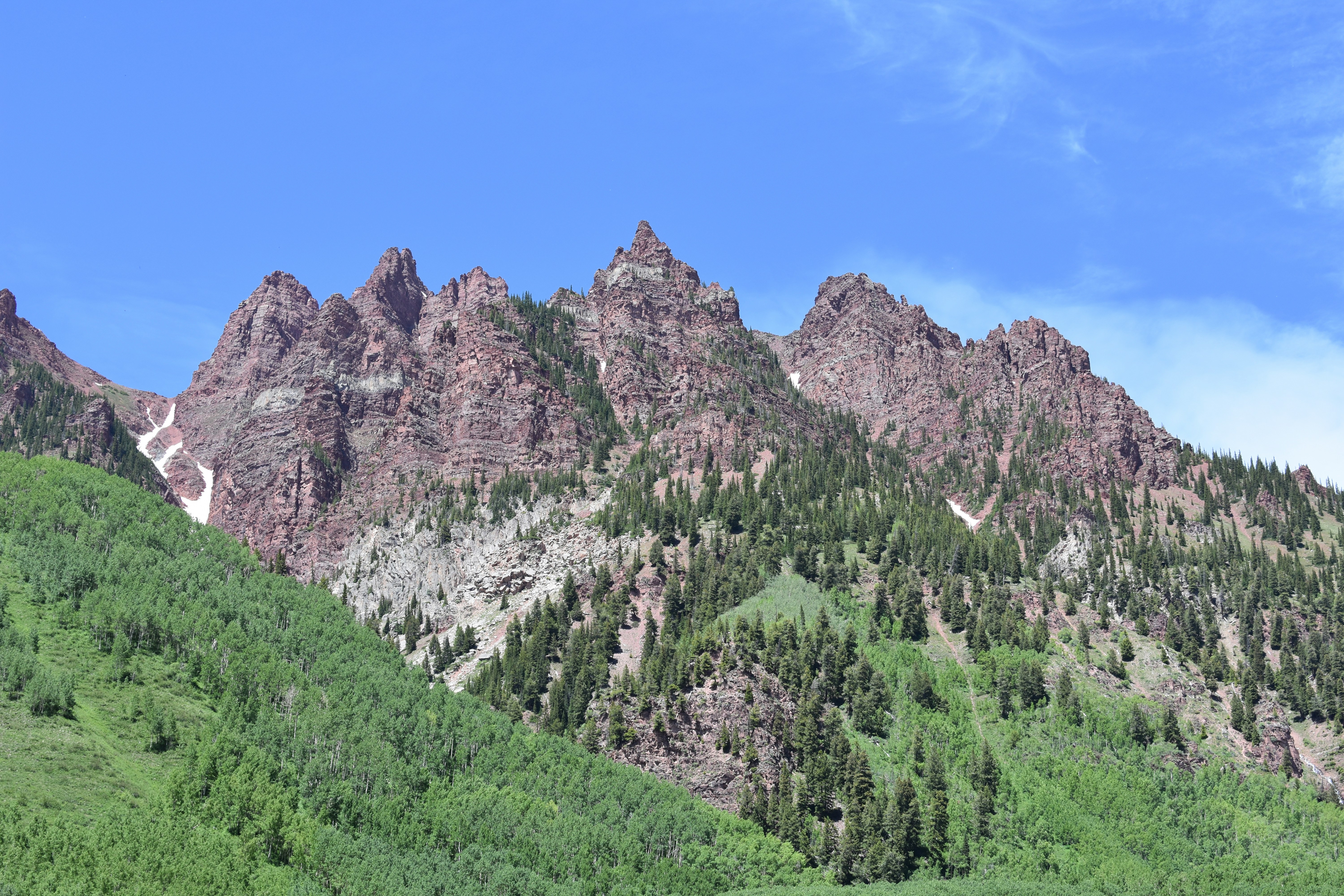 green trees near brown rocky mountain under blue sky during daytime