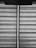 Horizontal blinds with a fabric texture are partially drawn, allowing a vertical sliver of light to pass through. A pull cord hangs from the upper portion of the blinds.