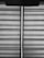 Horizontal blinds with a fabric texture are partially drawn, allowing a vertical sliver of light to pass through. A pull cord hangs from the upper portion of the blinds.