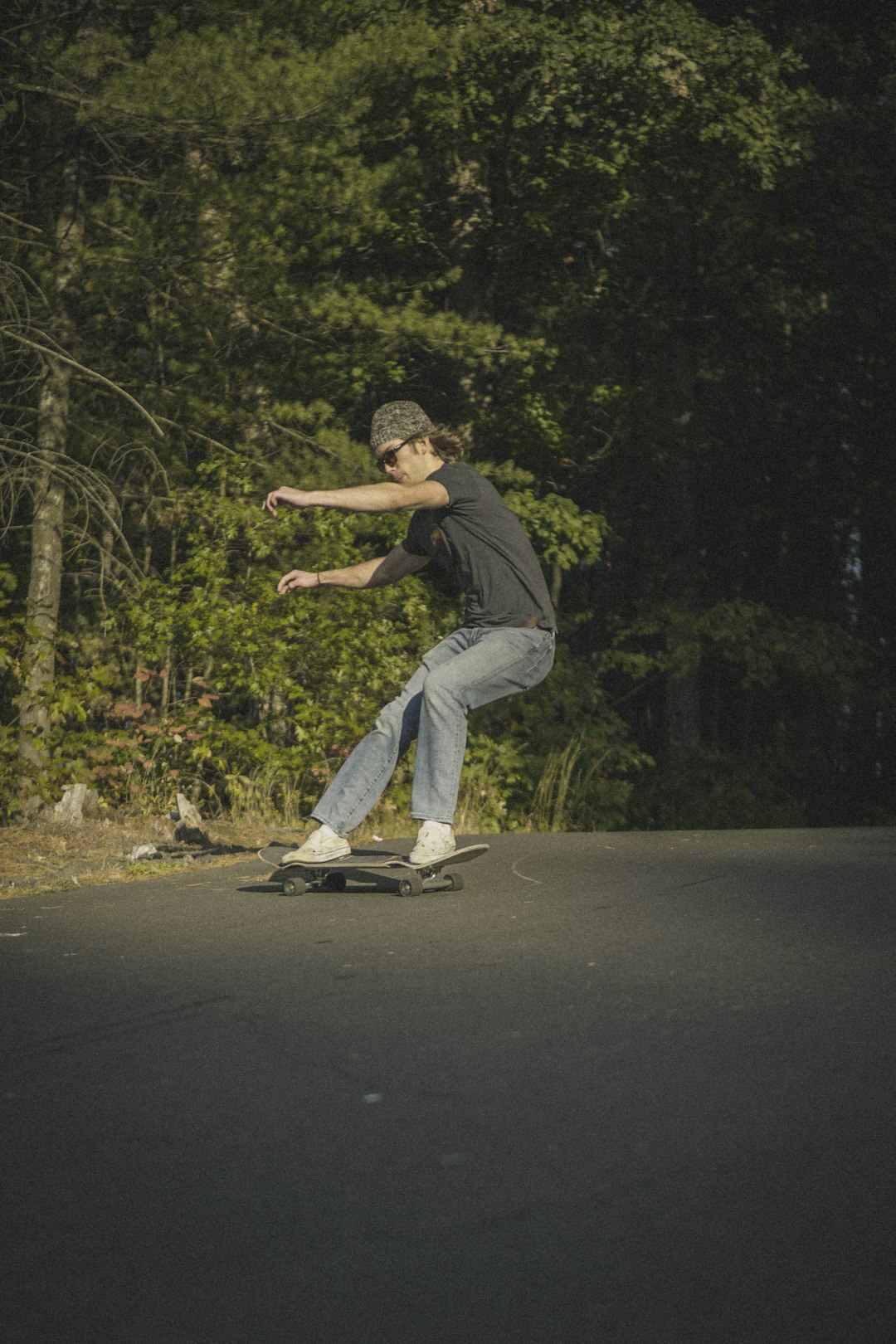 man in black t-shirt and blue denim jeans riding skateboard on road during daytime