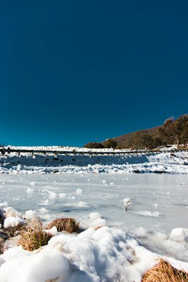A snow-covered roadside with a guardrail and snow gum trees under a deep blue sky at Thredbo
