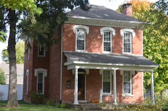 Classic colonial home painted warm brown with white pillars and autumn-toned landscaping.