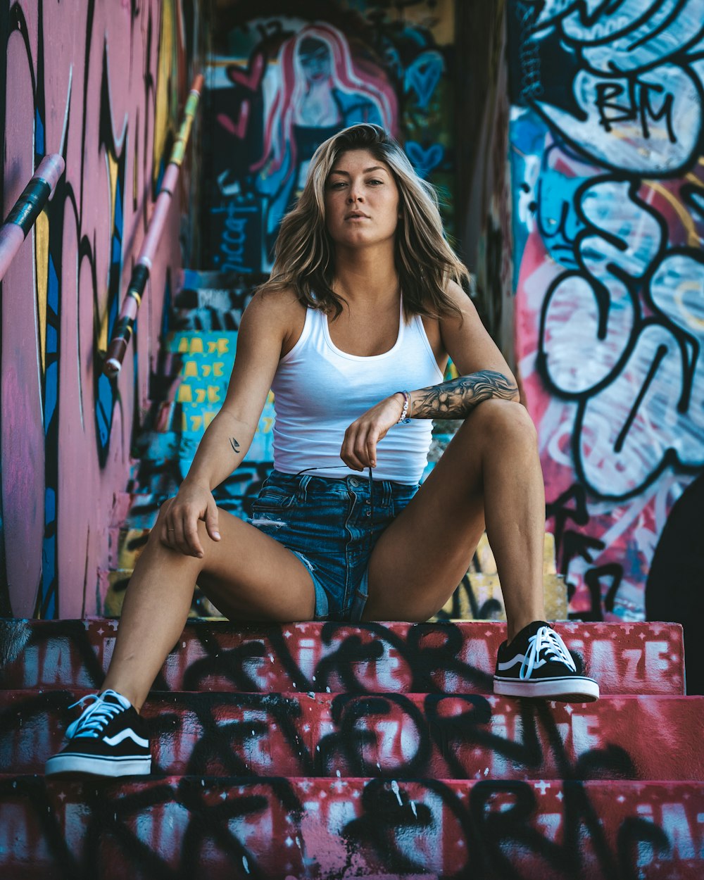 woman in white tank top and blue denim shorts sitting on red and white floral textile