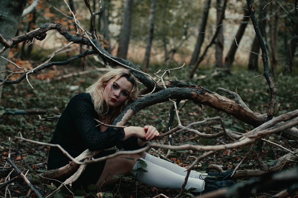 Femme en chemise noire à manches longues assise sur une branche d’arbre marron