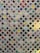 A quilt composed of numerous small, colorful fabric squares connected by a white lattice pattern. Each square features a unique design, ranging from polka dots and floral patterns to checkered designs. The quilt combines various colors including reds, greens, blues, and purples to create a vibrant patchwork effect.
