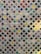 A quilt composed of numerous small, colorful fabric squares connected by a white lattice pattern. Each square features a unique design, ranging from polka dots and floral patterns to checkered designs. The quilt combines various colors including reds, greens, blues, and purples to create a vibrant patchwork effect.