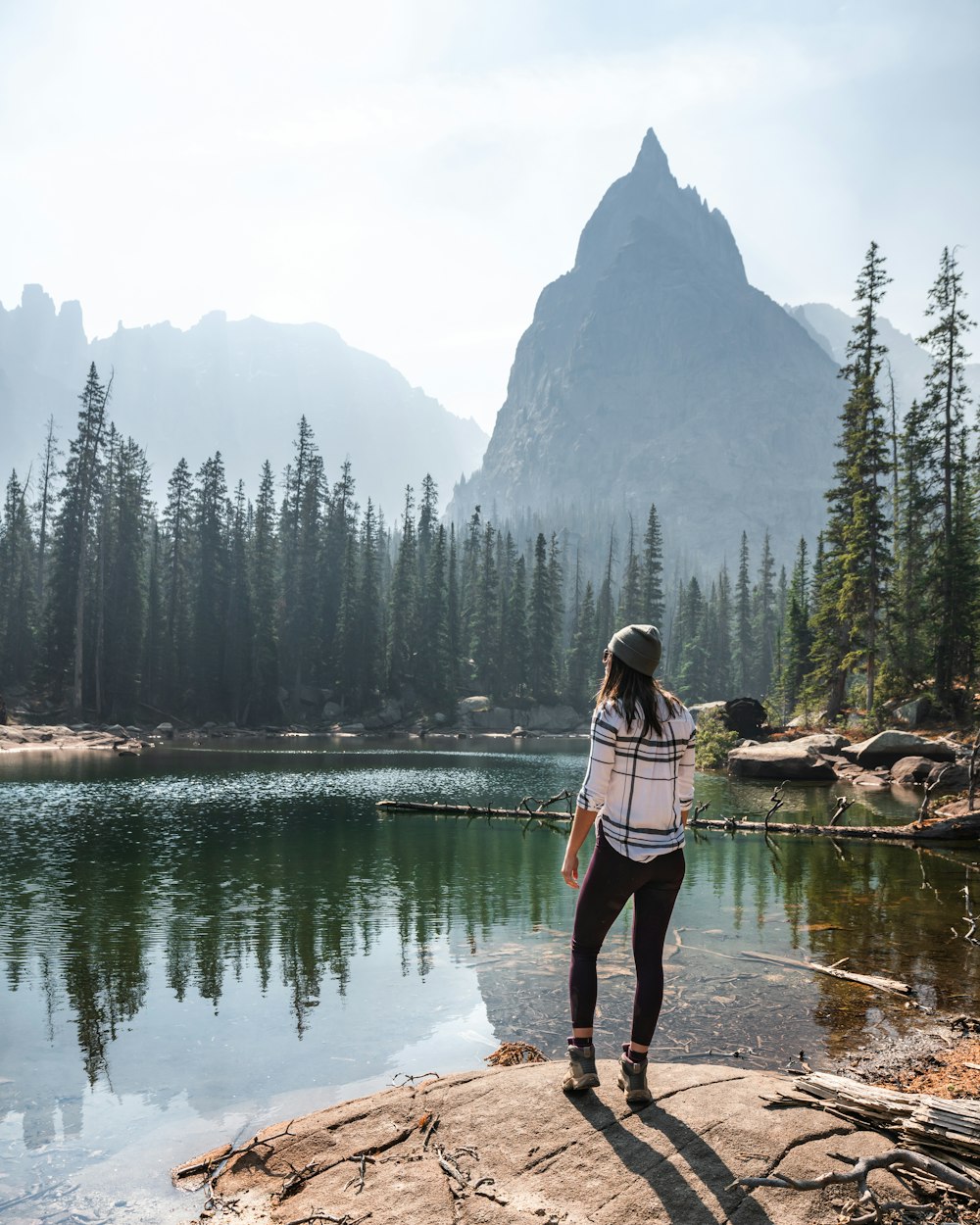 woman in pink jacket and black pants standing on rock near lake during daytime