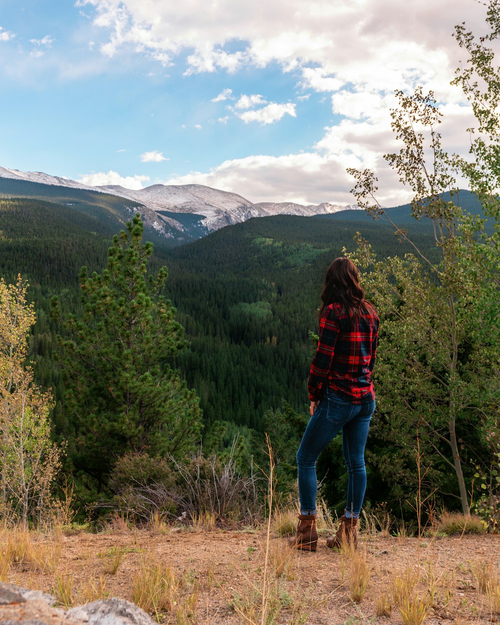 woman in red and black plaid jacket and blue denim jeans standing on brown grass field