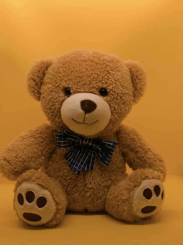 A hand-stitched teddy bear sitting on a nursery shelf beside books