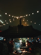 A group of women sharing laughter around a cozy fire pit under string lights in the evening.