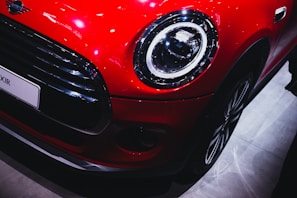 A close-up of a shiny red car's headlight reflecting sunlight on a clear day.