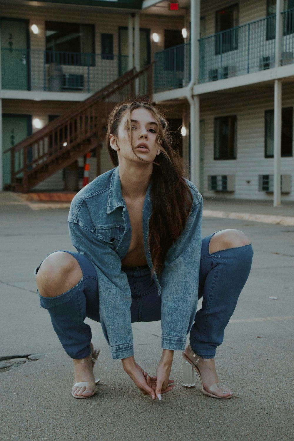 woman in blue denim jacket and blue denim jeans sitting on sidewalk during daytime