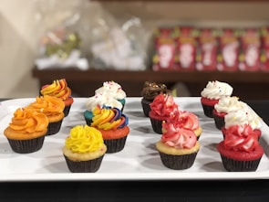 A variety of colorful cupcakes with smooth frosting arranged neatly on a modern white tray.