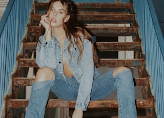 woman in blue denim jeans sitting on brown wooden staircase