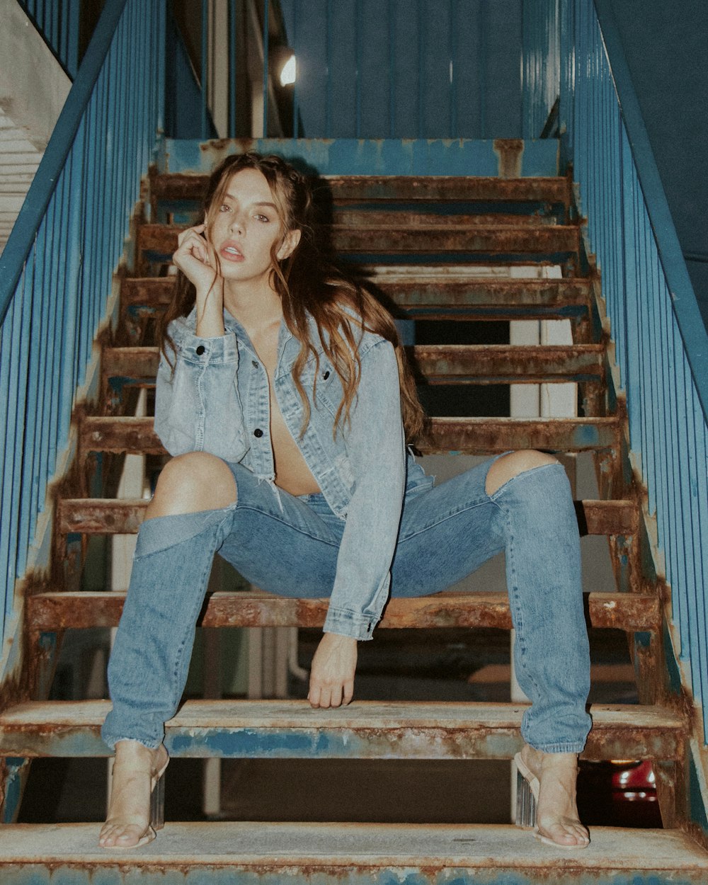 woman in blue denim jeans sitting on brown wooden staircase