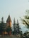 A red brick church with a pointed tower topped with a cross is situated among tall evergreen trees. The foreground includes a street with a traffic light and signage, contributing to a serene, small-town atmosphere.
