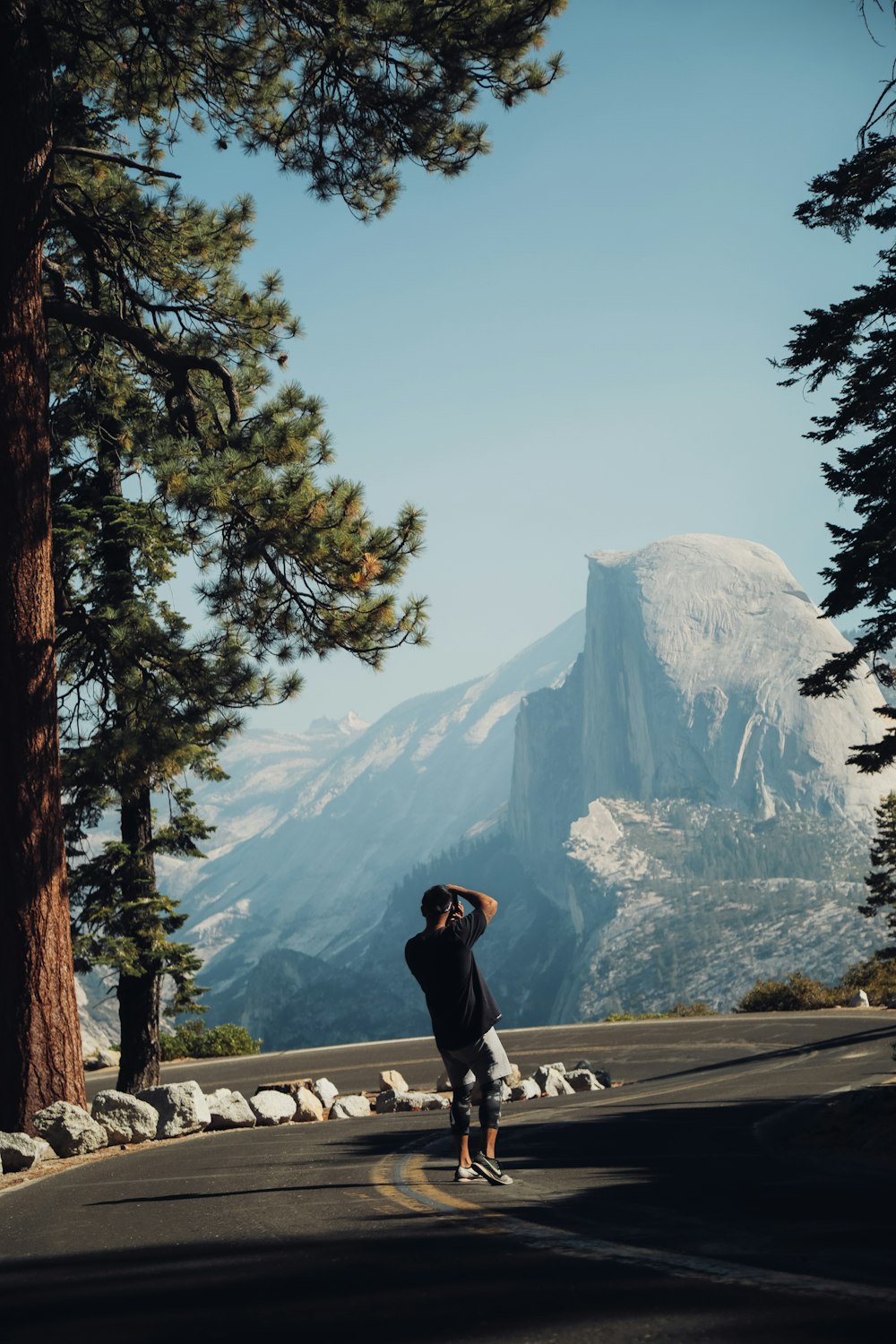 man in black jacket and black pants standing on gray concrete pavement near green trees and