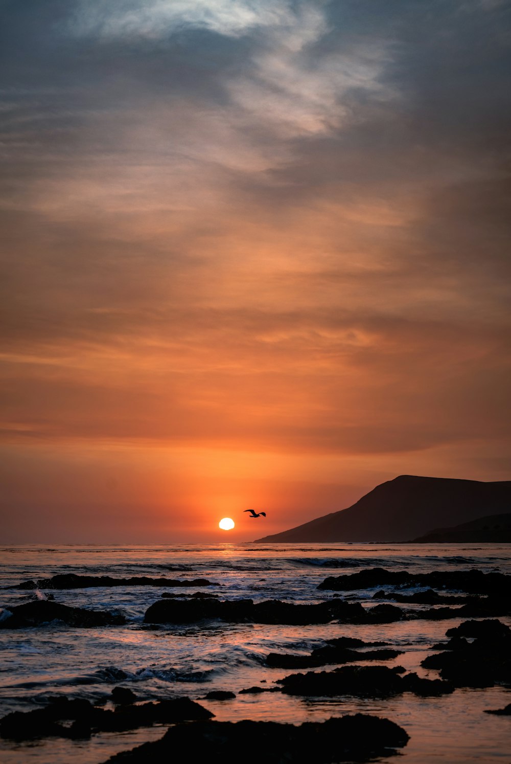 silhouette of mountain near body of water during sunset