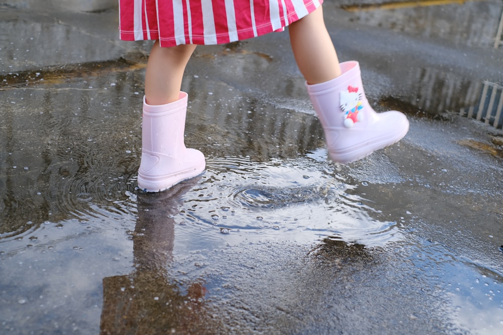 girl in white and pink polka dot dress and white boots standing on wet ground