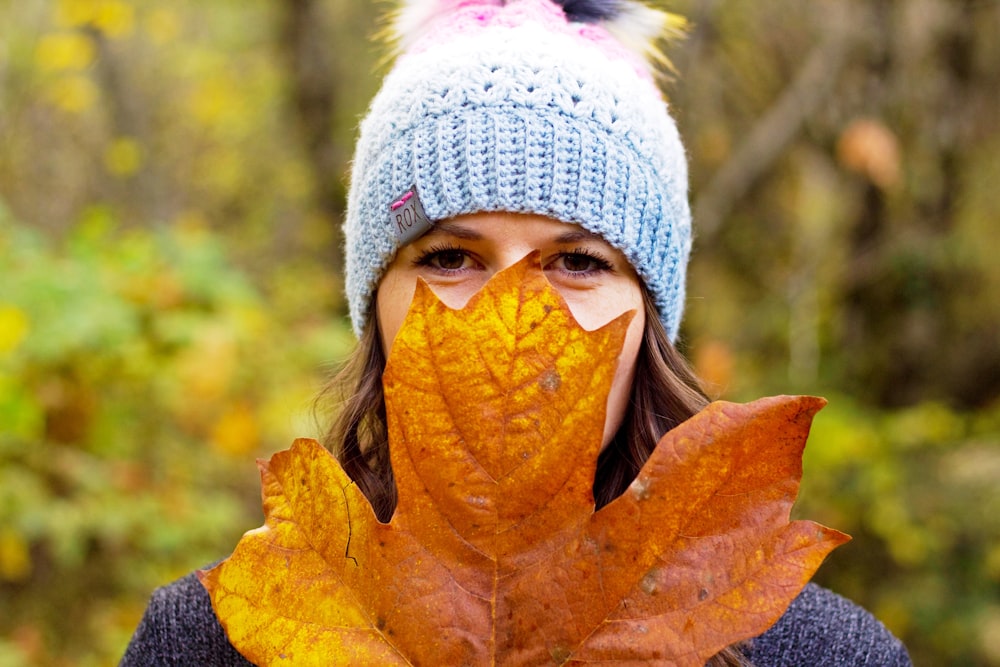 Femme en bonnet en tricot blanc couvrant son visage avec une feuille brune