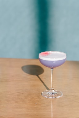 A moody, artistic shot of a glowing cocktail glass with orange and lavender hues against a dark background.