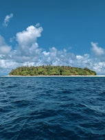 green island surrounded by blue sea under blue and white cloudy sky during daytime
