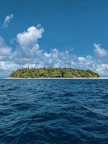 green island surrounded by blue sea under blue and white cloudy sky during daytime