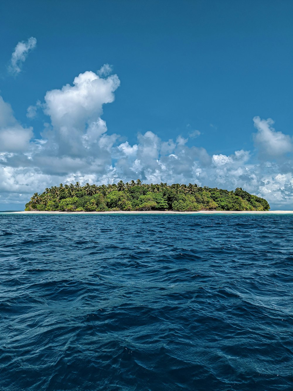 ilha verde cercada por mar azul sob céu nublado azul e branco durante o dia