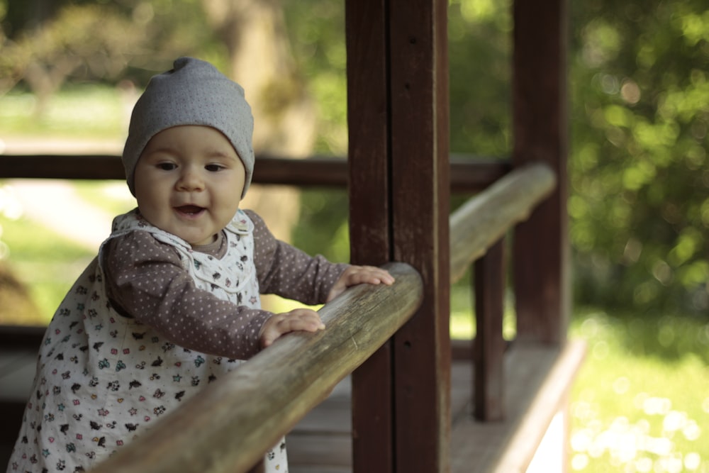 baby in gray and white polka dot onesie sitting on brown wooden swing during daytime