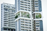 Modern high-rise residential buildings with a unique architectural design featuring prominent balconies and integrated greenery. The structures have a geometric pattern with large windows and white, sleek facades.