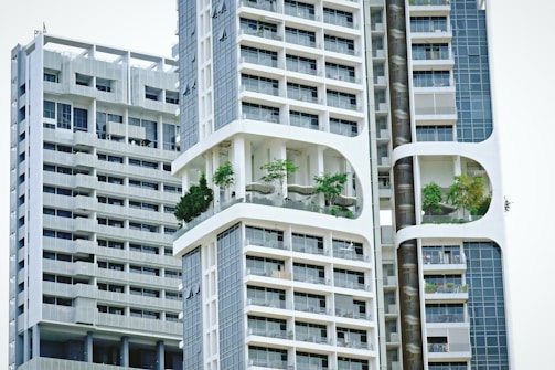 Modern high-rise residential buildings with a unique architectural design featuring prominent balconies and integrated greenery. The structures have a geometric pattern with large windows and white, sleek facades.