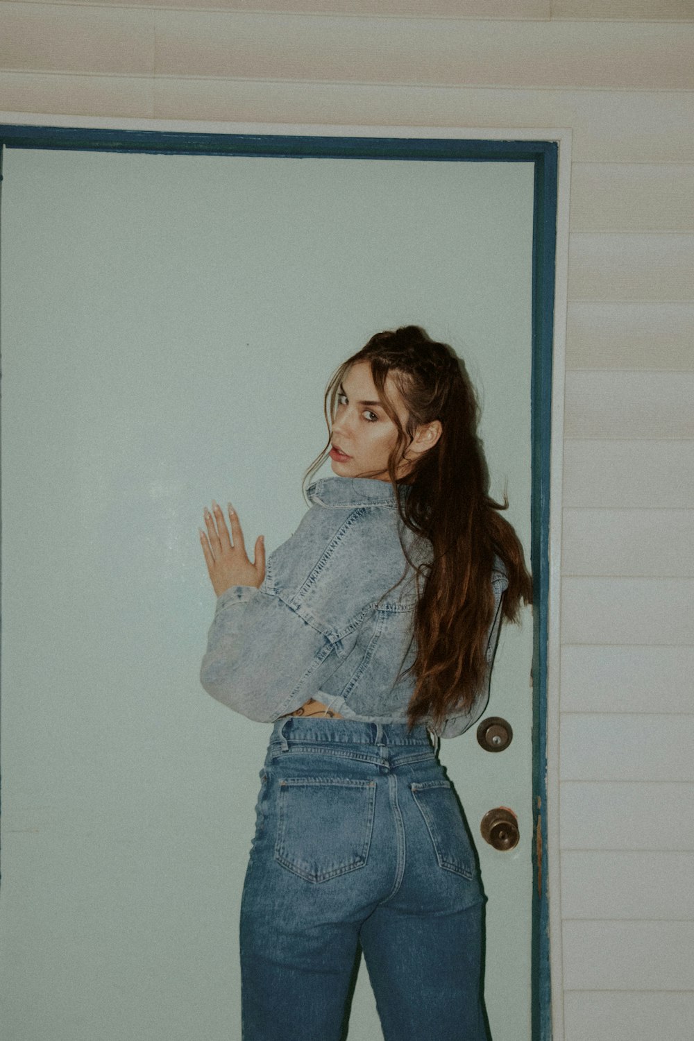 girl in blue denim jacket and blue denim shorts standing beside white wooden door