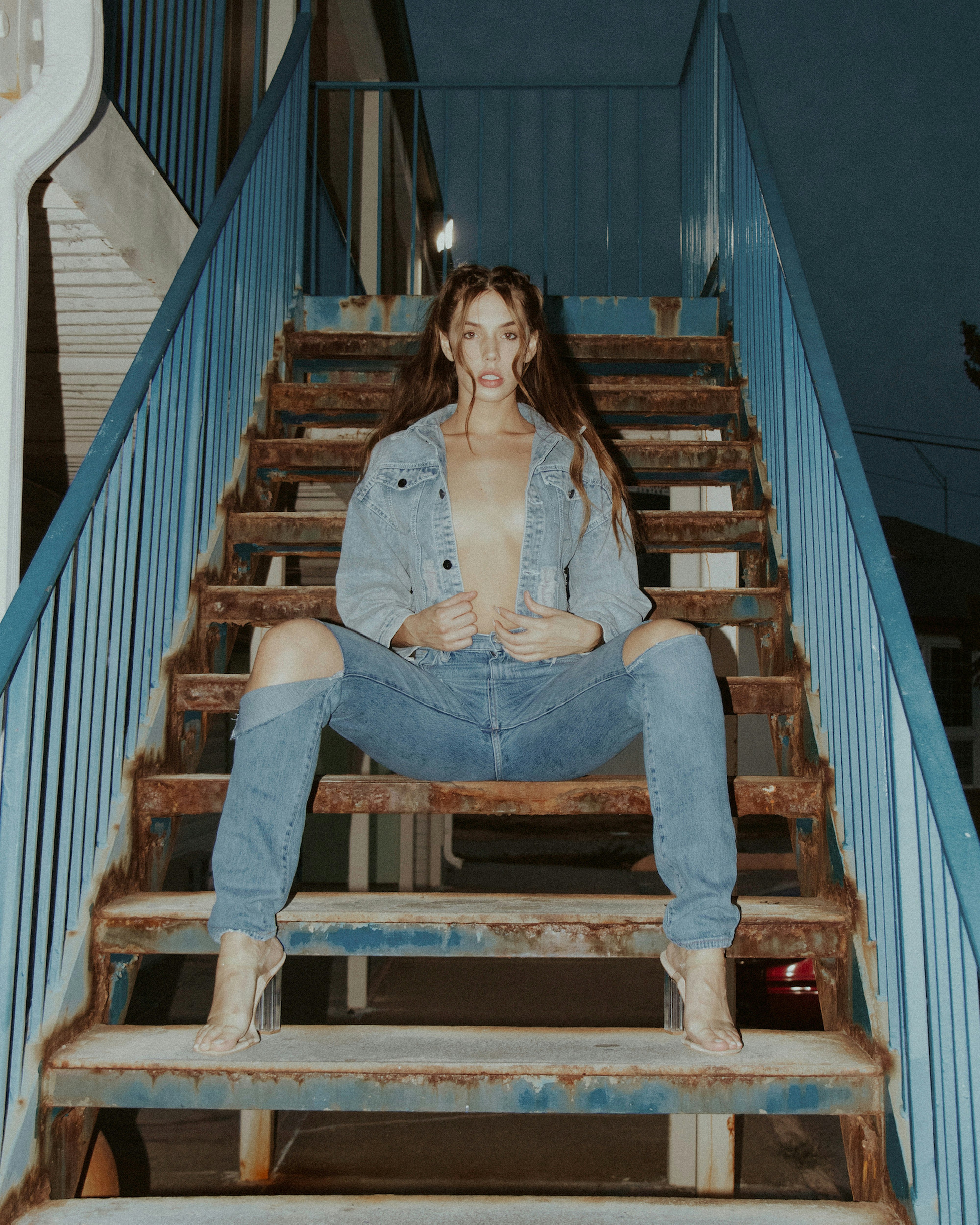 woman in white shirt and blue denim jeans sitting on brown wooden staircase