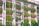 A building facade with pink walls features numerous vertical green gardens. Lush plants and vines cascade down from multiple levels, integrated into the structure's design, creating a living wall effect. Trees line the base, enhancing the natural aesthetics.