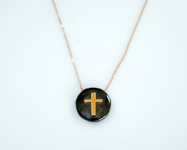A pendant featuring a gold cross design set against a glossy dark background, suspended on a delicate gold chain.