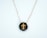 A pendant featuring a gold cross design set against a glossy dark background, suspended on a delicate gold chain.