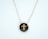 A pendant featuring a gold cross design set against a glossy dark background, suspended on a delicate gold chain.
