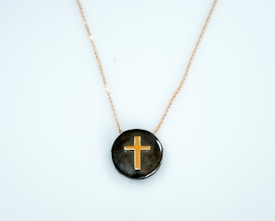 A pendant featuring a gold cross design set against a glossy dark background, suspended on a delicate gold chain.