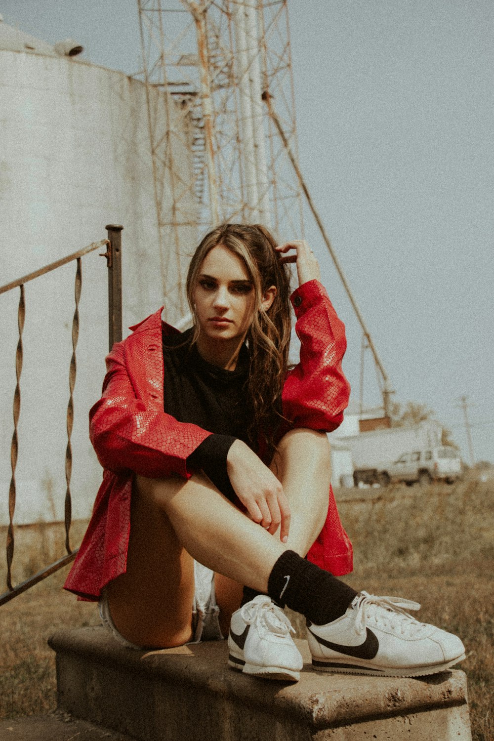 woman in red and black long sleeve shirt and black shorts sitting on brown wooden fence