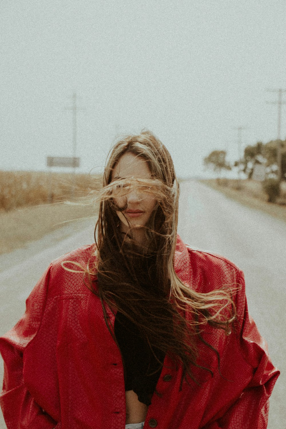 woman in red jacket standing on road during daytime